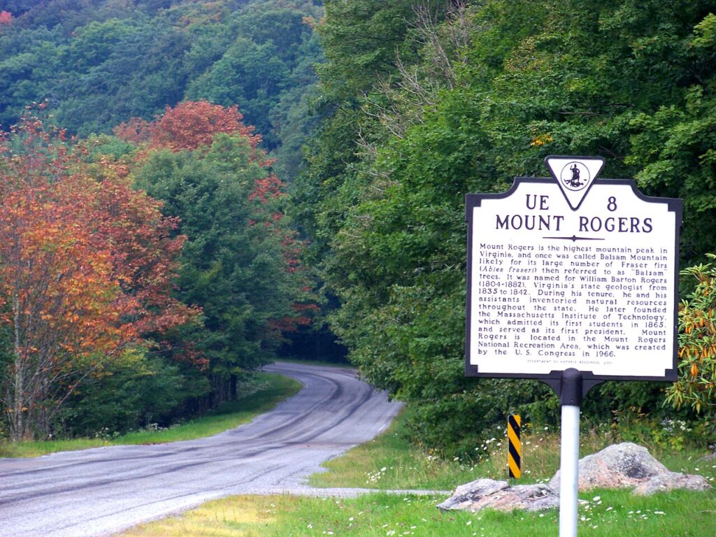 Sign for Mount Rogers, Virginia's highest peak, surrounded by colorful trees along a winding road.