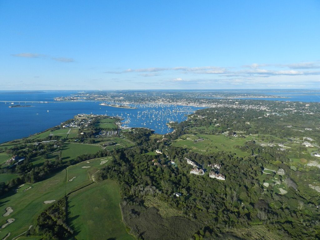 Aerial view of a coastal town featuring lush green hills, a bay filled with boats, and a clear blue sky.