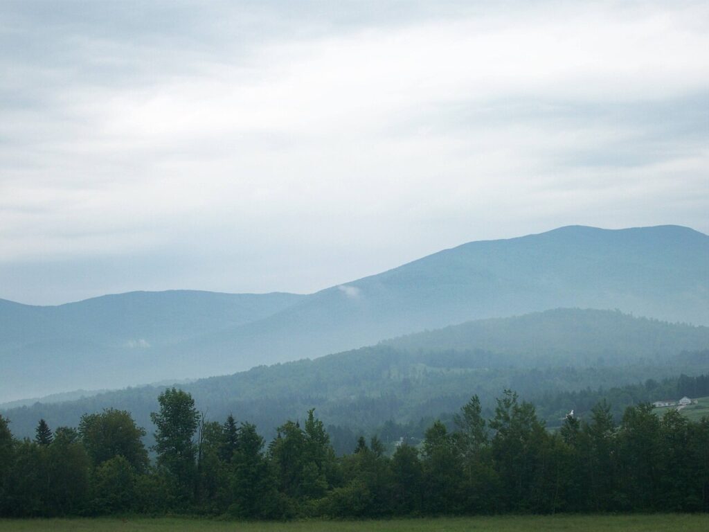 Foggy mountains rise gently in the background, surrounded by lush greenery under a cloudy sky.
