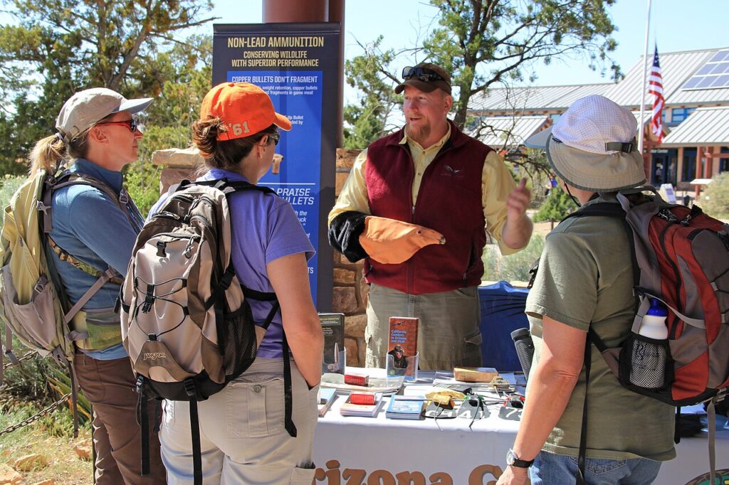 A group discussions with a guide at an outdoor booth promoting non-lead ammunition for wildlife conservation.