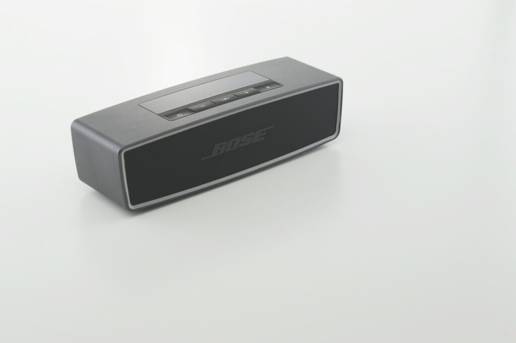 A sleek, gray Bose Bluetooth speaker with control buttons on top, positioned on a minimalistic white background.