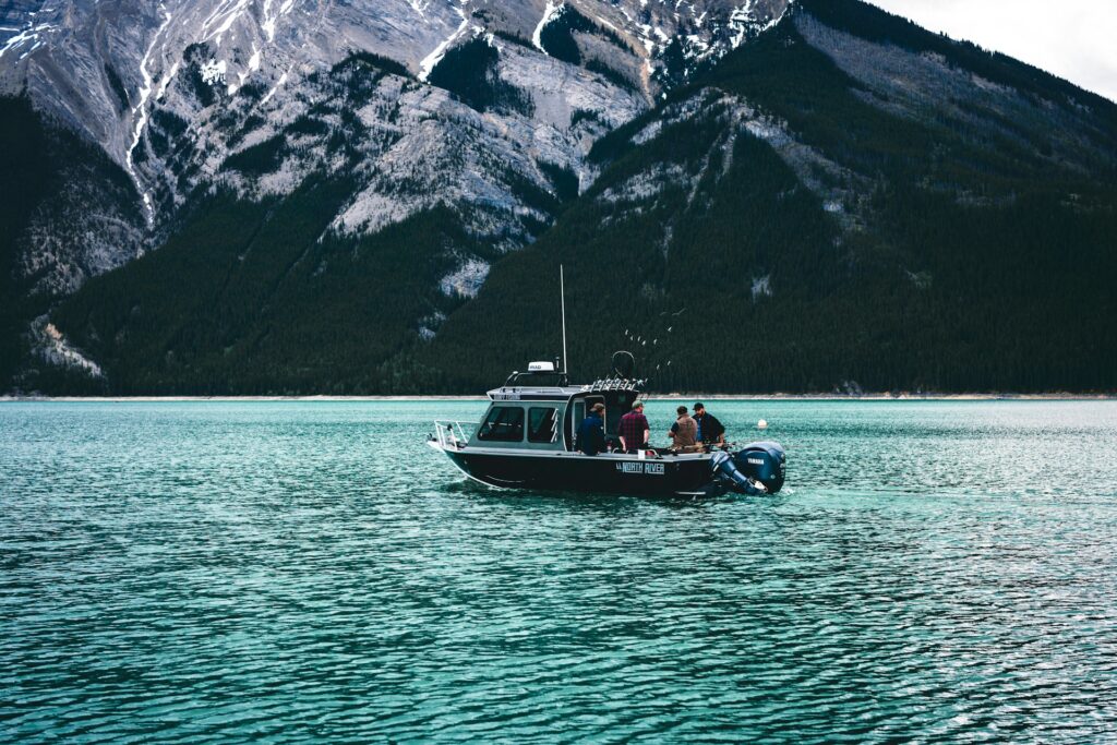 A fishing boat with several people is anchored on turquoise water, surrounded by majestic mountains, creating a tranquil outdoor scene.