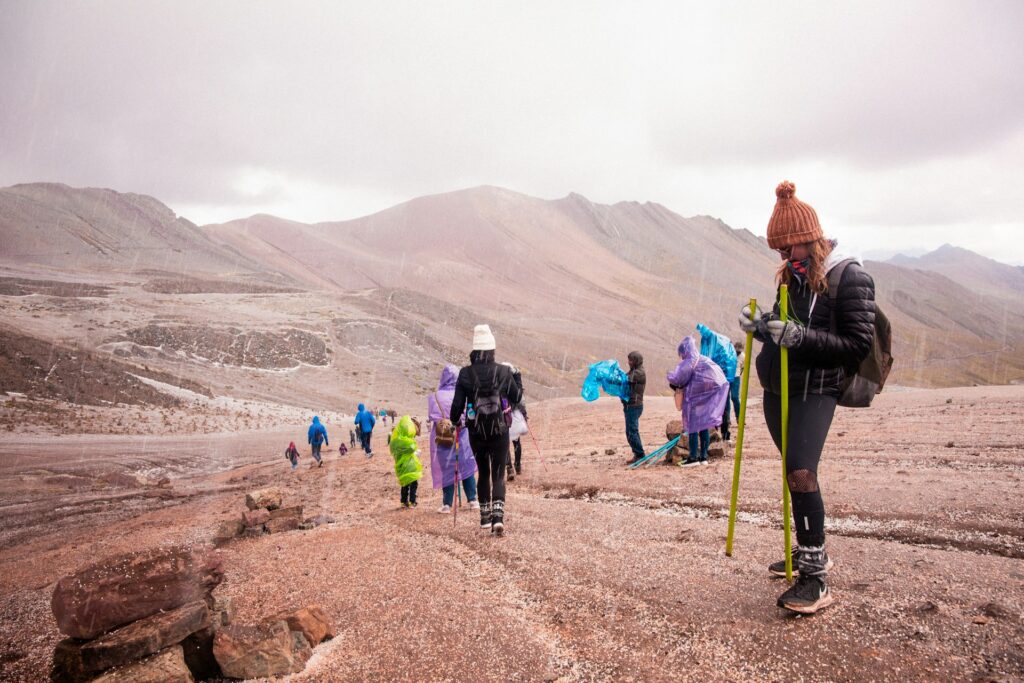 A group of hikers dressed in colorful rain gear traverses a rocky, mountainous landscape during a rain shower.