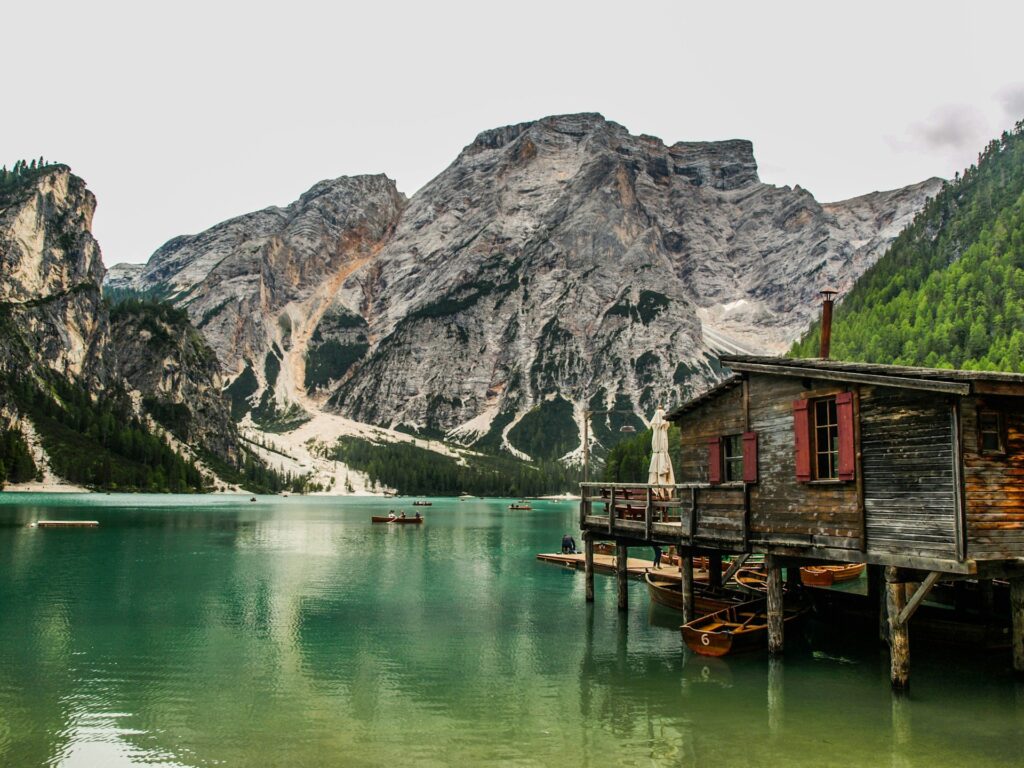 A serene alpine scene featuring a wooden boathouse by a turquoise lake, surrounded by towering mountains and lush greenery.