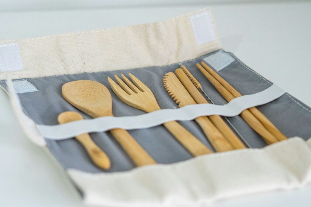 A roll-up storage pouch containing various bamboo utensils: a spoon, fork, knife, and chopsticks on a gray fabric background.