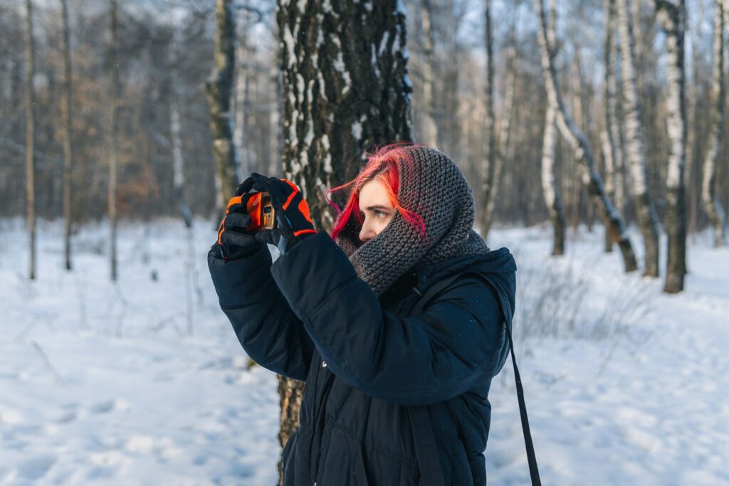 A woman with red hair is taking a photo with her smartphone, smiling as she captures the moment.