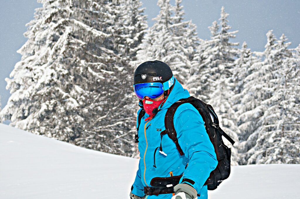 A skier in a bright blue jacket and black helmet navigates a snowy landscape, surrounded by frosted trees in a winter scene.