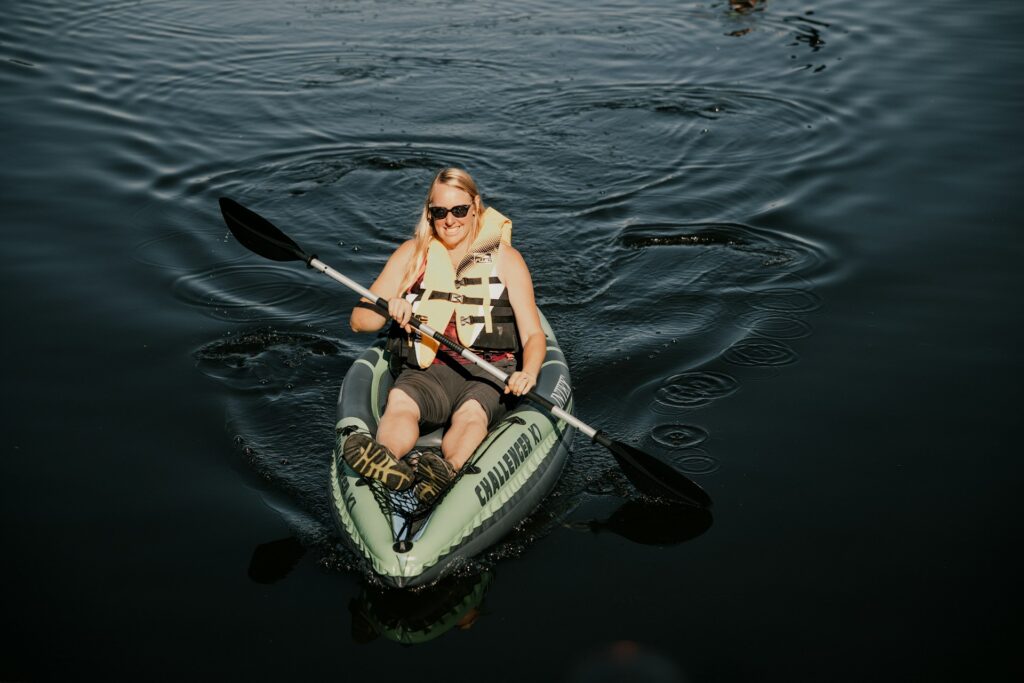 A person paddles a green inflatable kayak on dark, rippling water, wearing a life jacket and enjoying a leisurely outing.