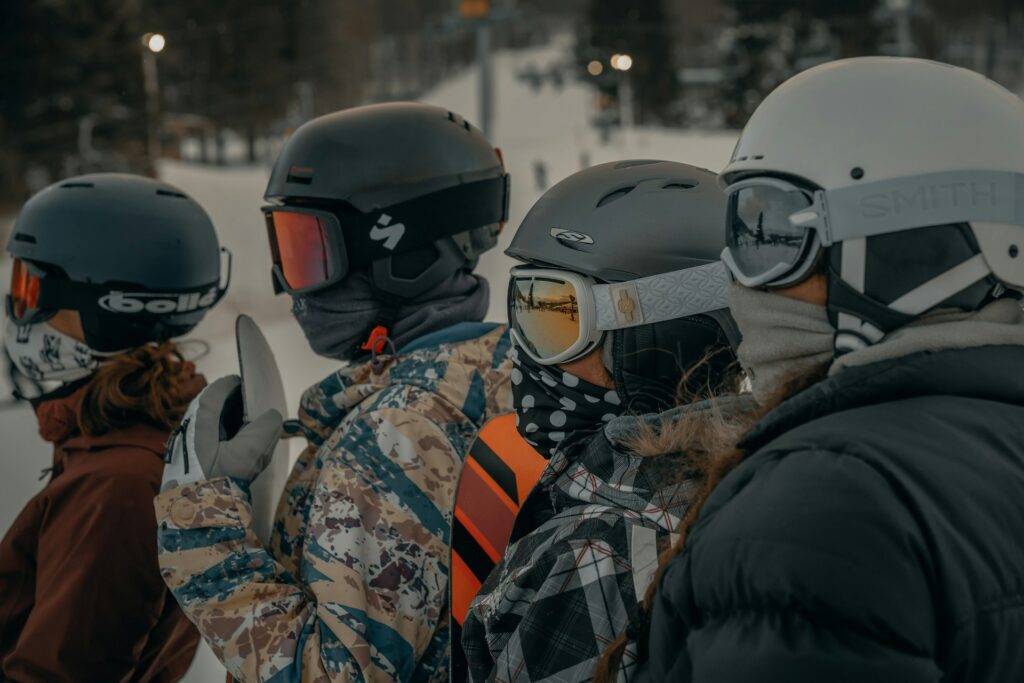 Four skiers in helmets and goggles line up at a snowy slope, preparing for their descent on a winter day.