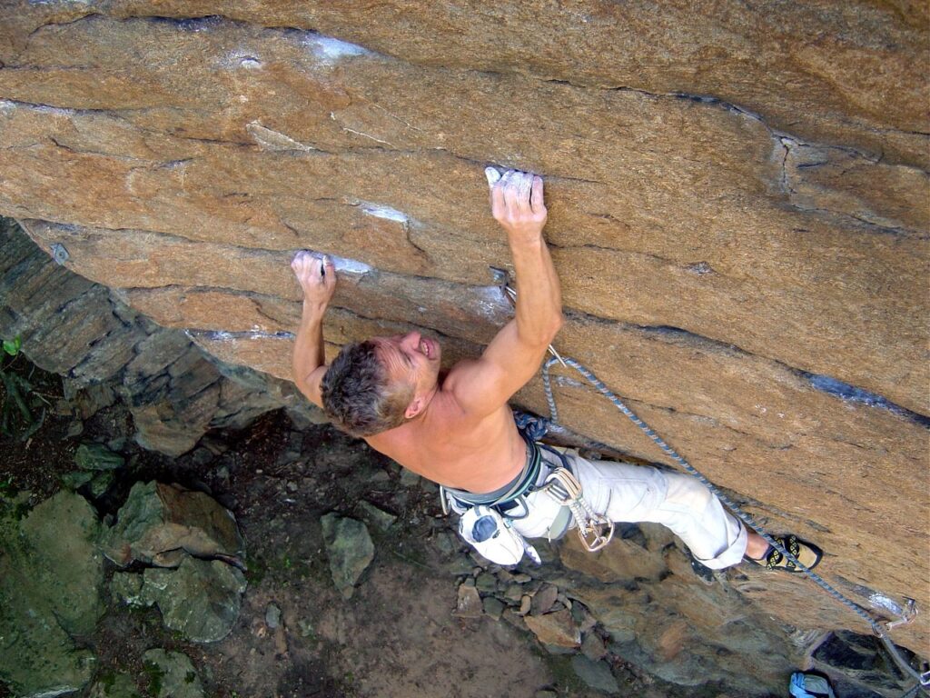 A climber ascends a rocky cliff, gripping the holds with chalked hands, showcasing determination and focus against a natural backdrop.