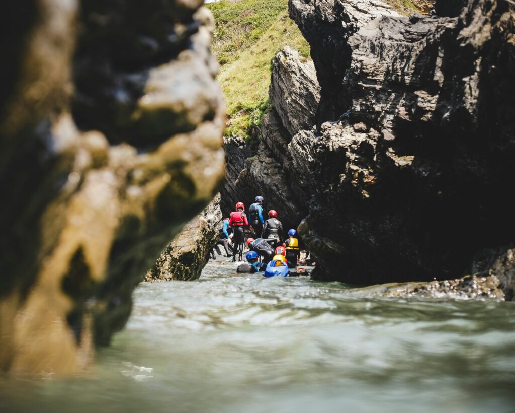 A group of adventurers in wetsuits navigating a narrow waterway between rugged rocks, enjoying a day of coastal exploration.