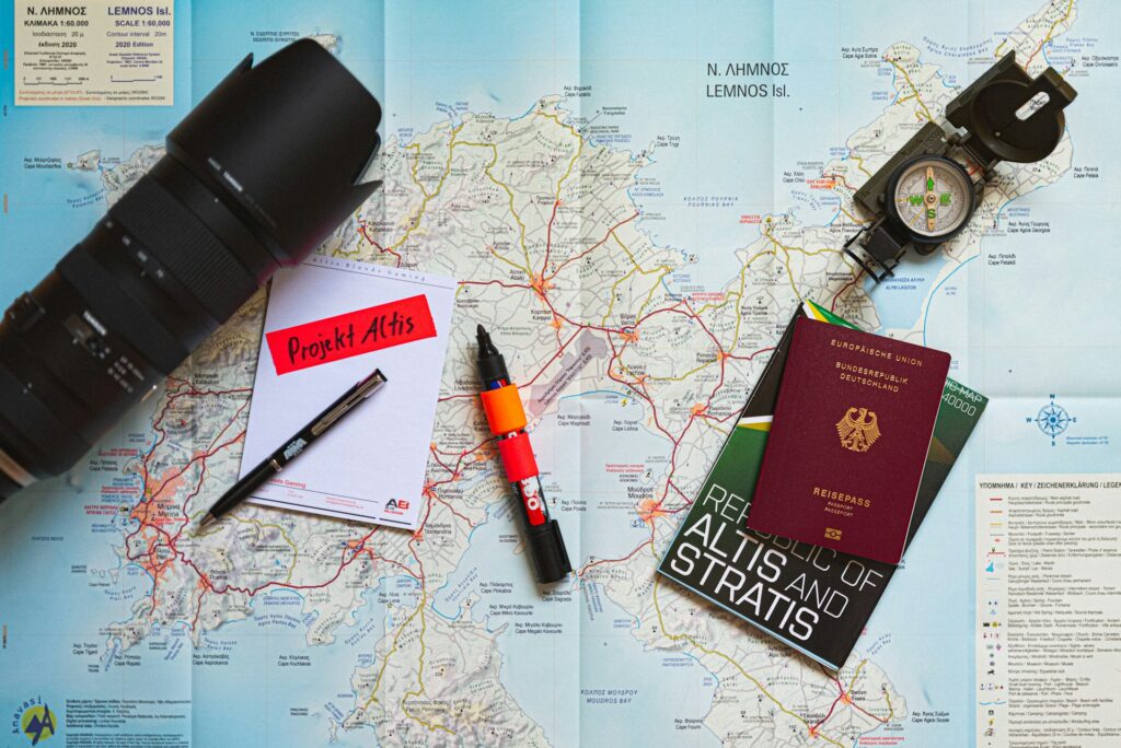 A camera, map of Lemnos, project notes, compass, and German passport arranged for travel planning.