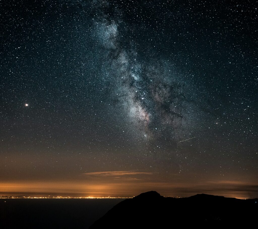 The Milky Way and Venus shine brightly over a calm ocean at night, creating a stunning celestial view.