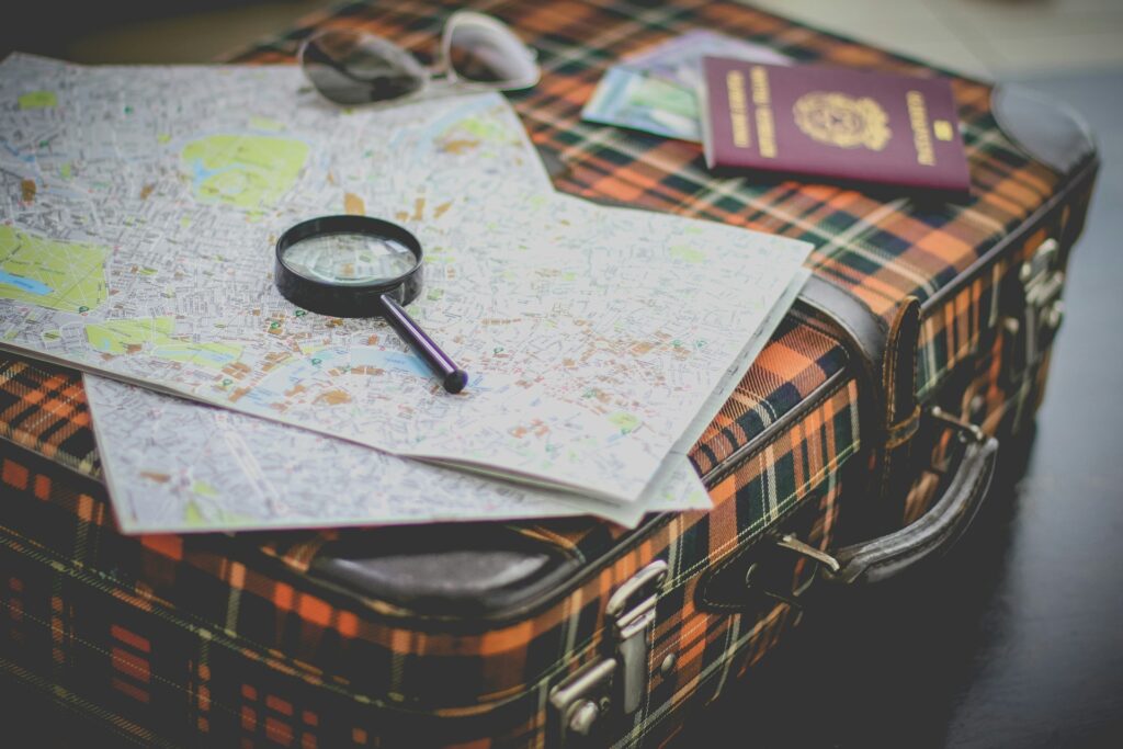 A vintage suitcase with a map, magnifying glass, passport, and sunglasses on a table, symbolizing travel planning and adventure.