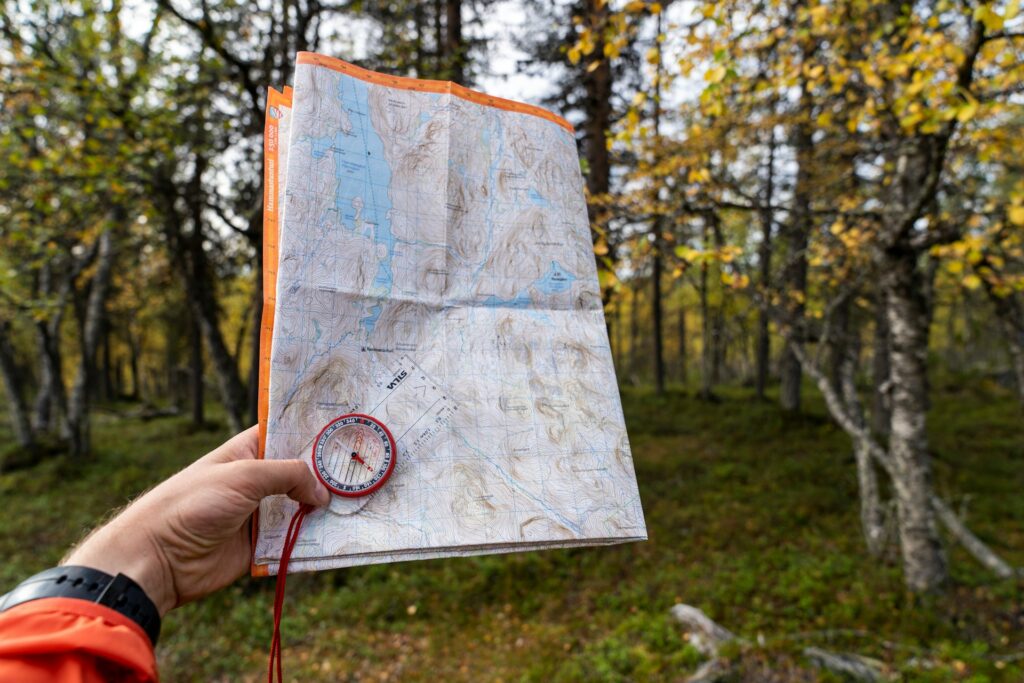A person holds a detailed topographic map and compass, surrounded by a forest with autumn foliage.