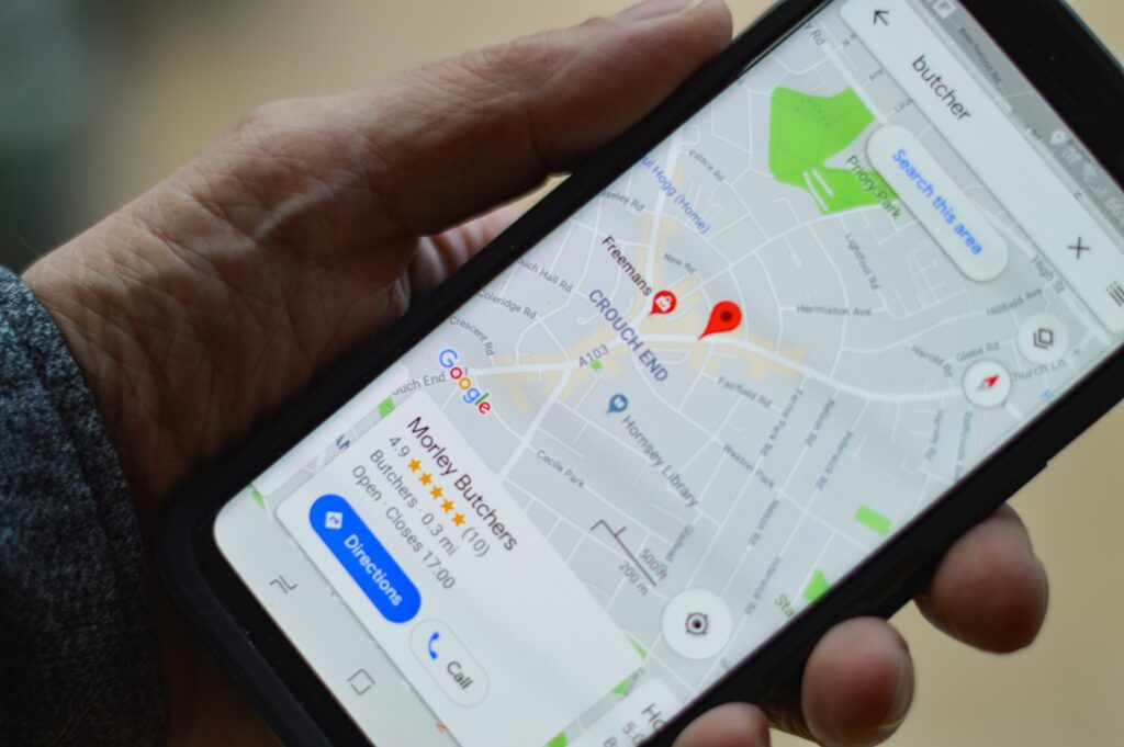 A person holds a smartphone displaying a Google Maps location for "Morley Butchers" in Crouch End, showing directions and rating.