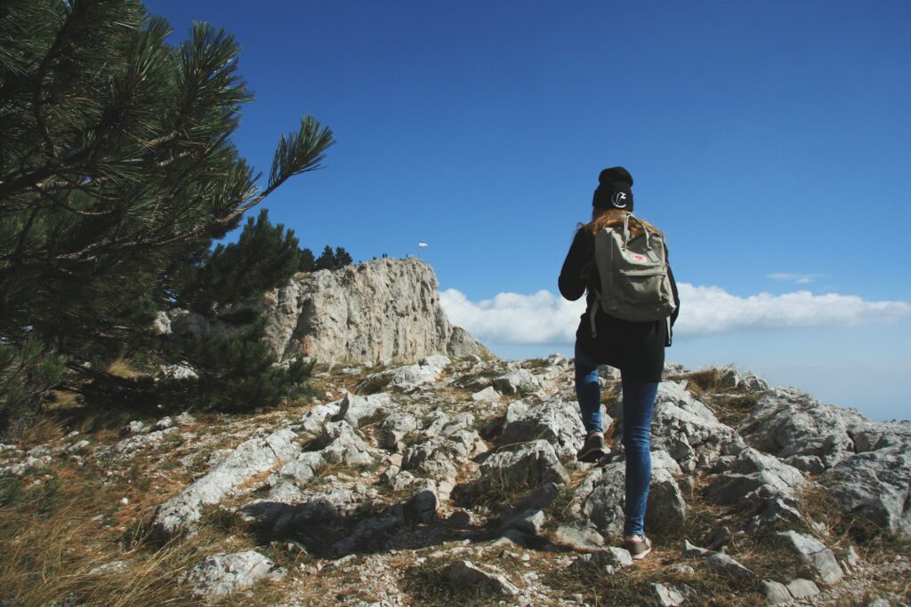A woman with long hair stands on a rock, gazing at lush green mountains under a cloudy sky.