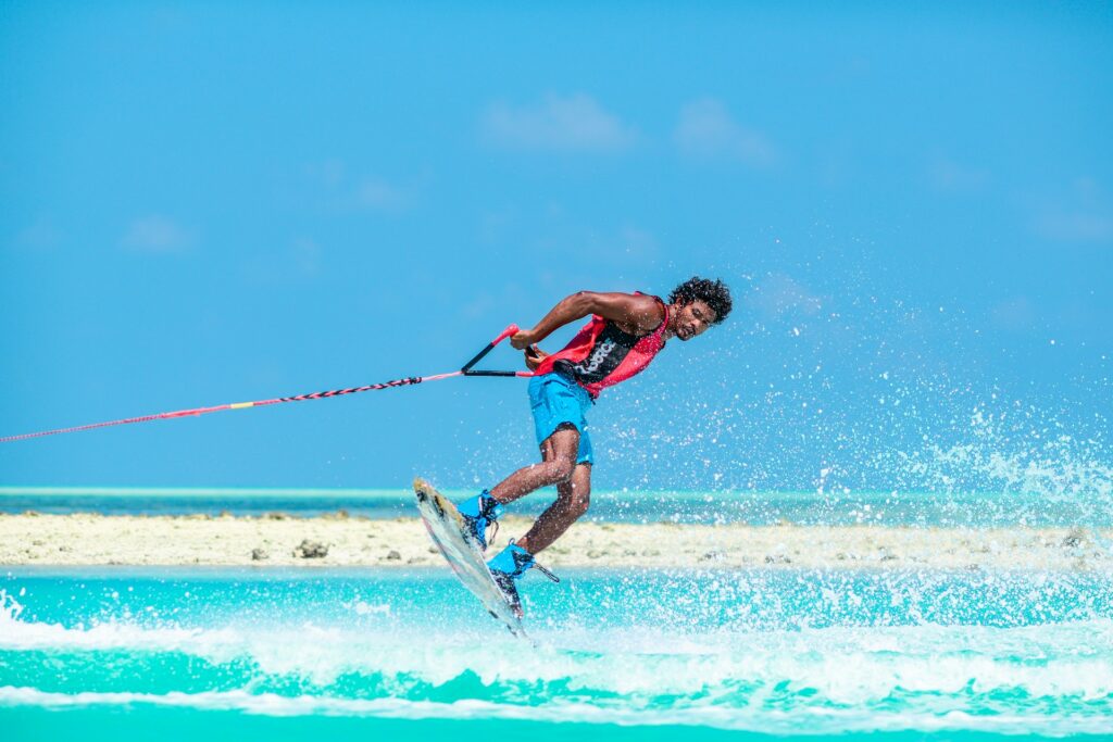 A young man performs a dynamic trick while water skiing on a bright, turquoise lagoon under a clear blue sky.