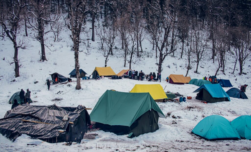 A winter camping scene with colorful tents surrounded by snow-covered ground and trees, featuring people gathering in the background.