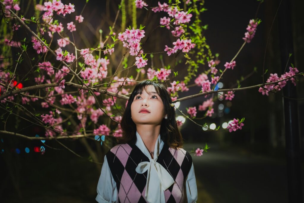 a woman standing in front of a tree with pink flowers