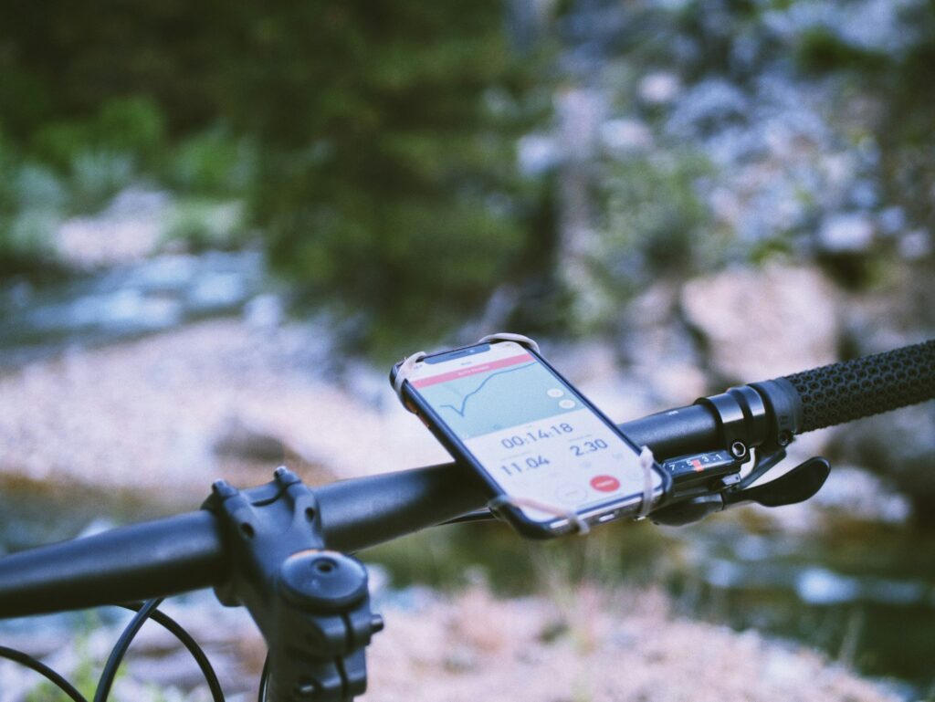 Smartphone displaying biking stats mounted on a bike handlebar, with a blurred background of a river and foliage.