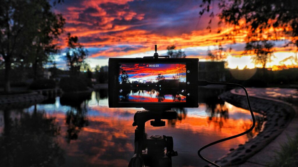 A camera mounted on a tripod is positioned in front of a serene lake, capturing the tranquil landscape.
