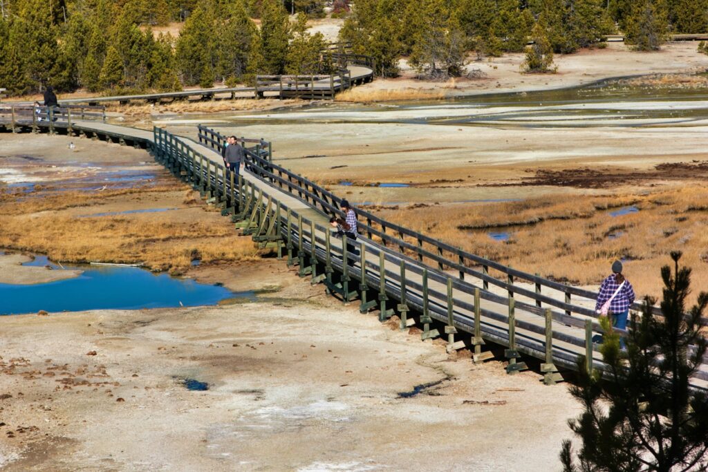 A wooden boardwalk stretches through a dry, grassy landscape, with several people walking and enjoying the scenic surroundings.