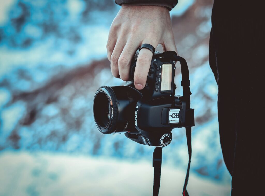 A person holds a Canon DSLR camera in one hand against a blurred, icy background, showcasing a passion for photography in winter.