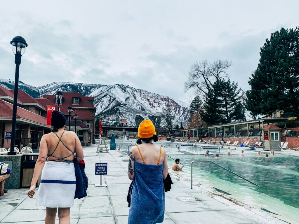 Two women stroll by a pool with mountains rising majestically in the background.
