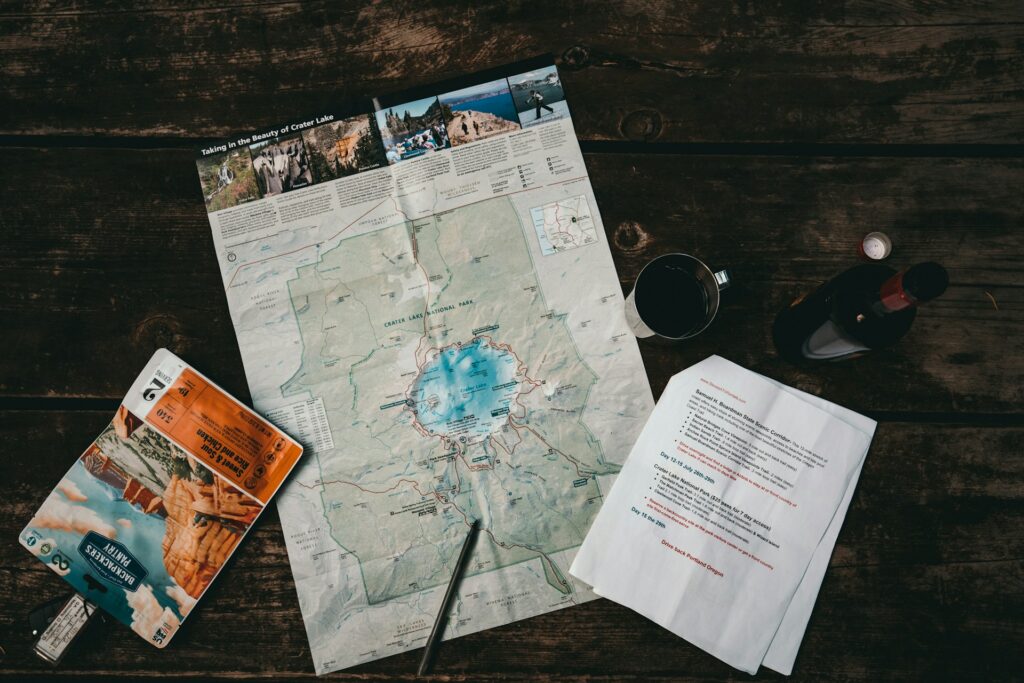 A Crater Lake map and itinerary are spread on a wooden table, accompanied by a coffee cup and a wine bottle.