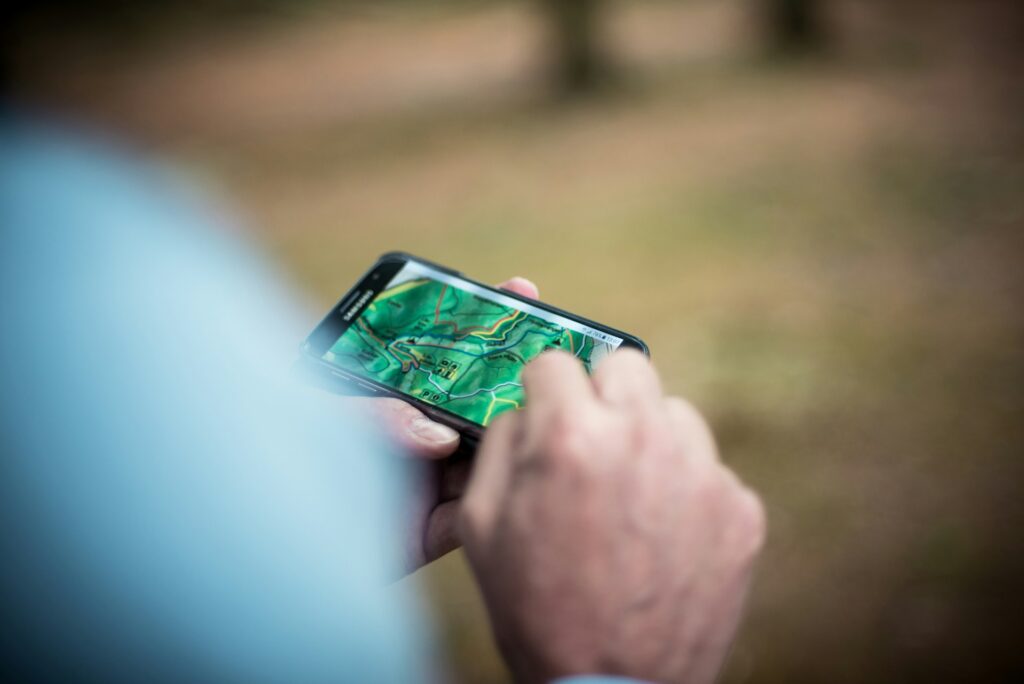 A close-up of a person's hand using a smartphone displaying a detailed map, set against a blurred natural background.
