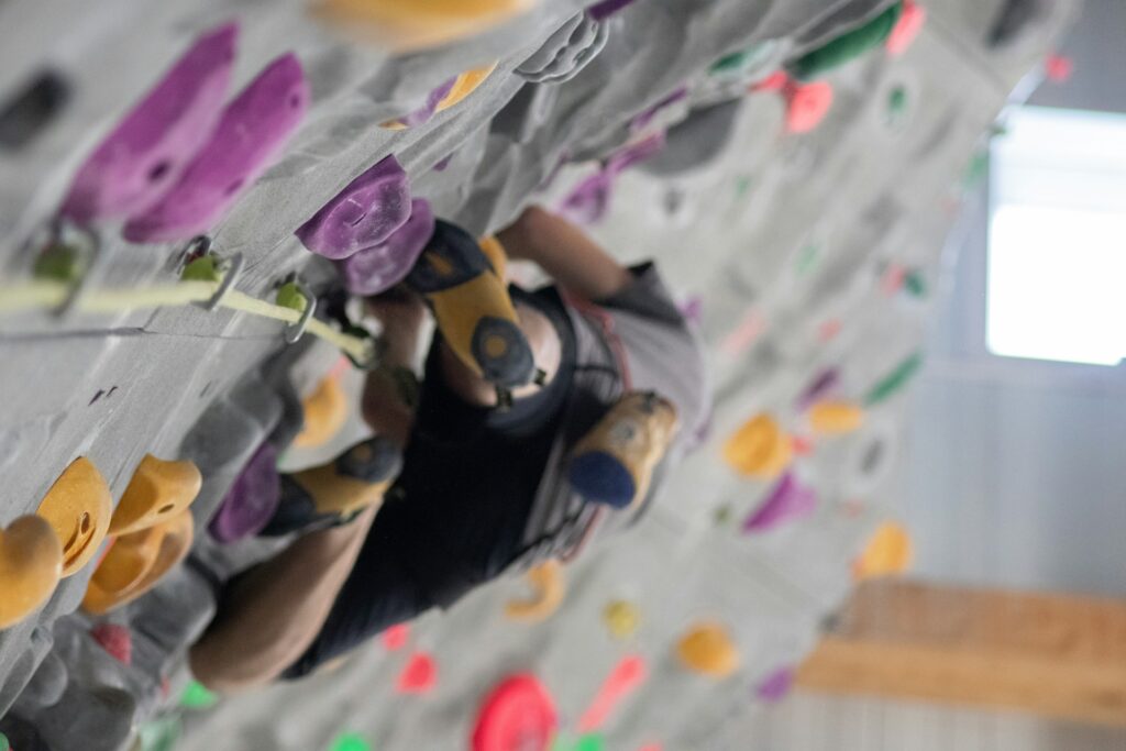 A climber scales a colorful indoor rock wall, focusing on their foot placement and hand grips while using climbing gear.