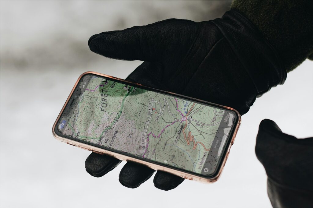 A gloved hand holds a smartphone displaying a detailed topographic map, set against a snowy background.