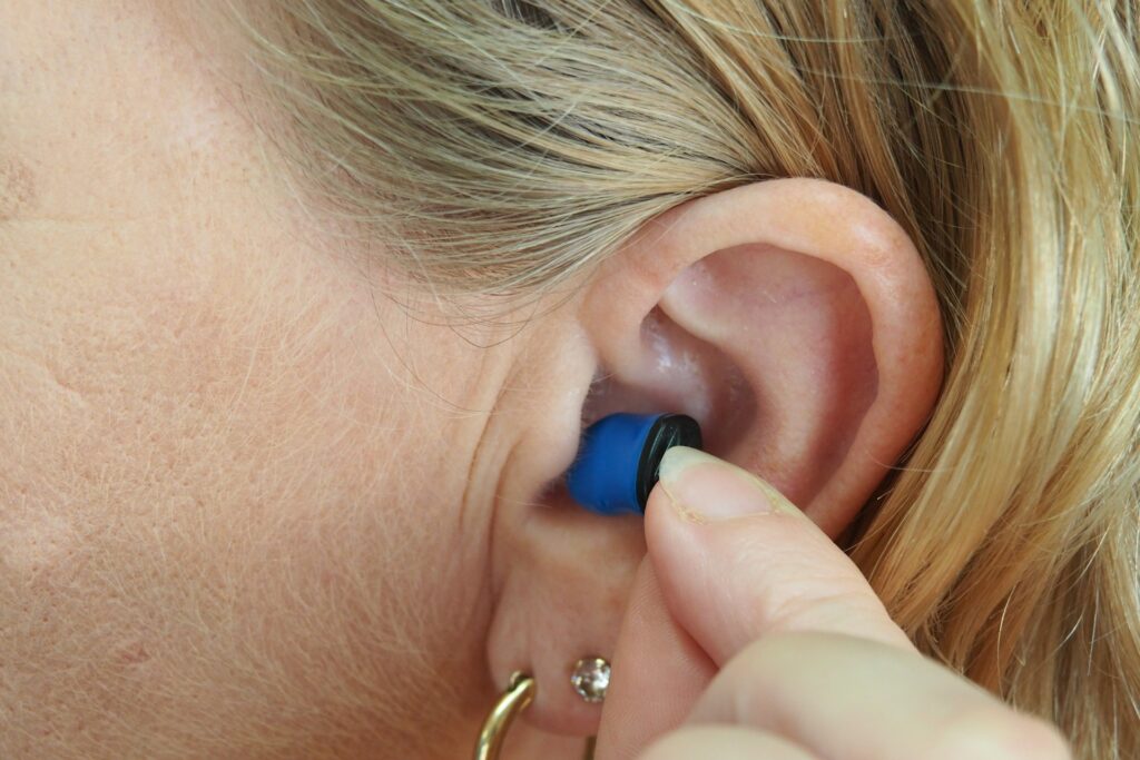 A close-up of a woman's ear as she inserts a blue and black earplug, highlighting her ear and hair.