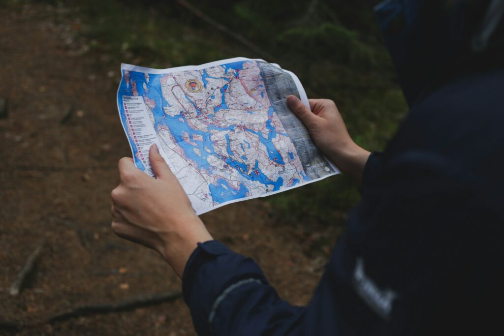 A person holds a detailed map with blue waterways and trails, navigating through a forested area.