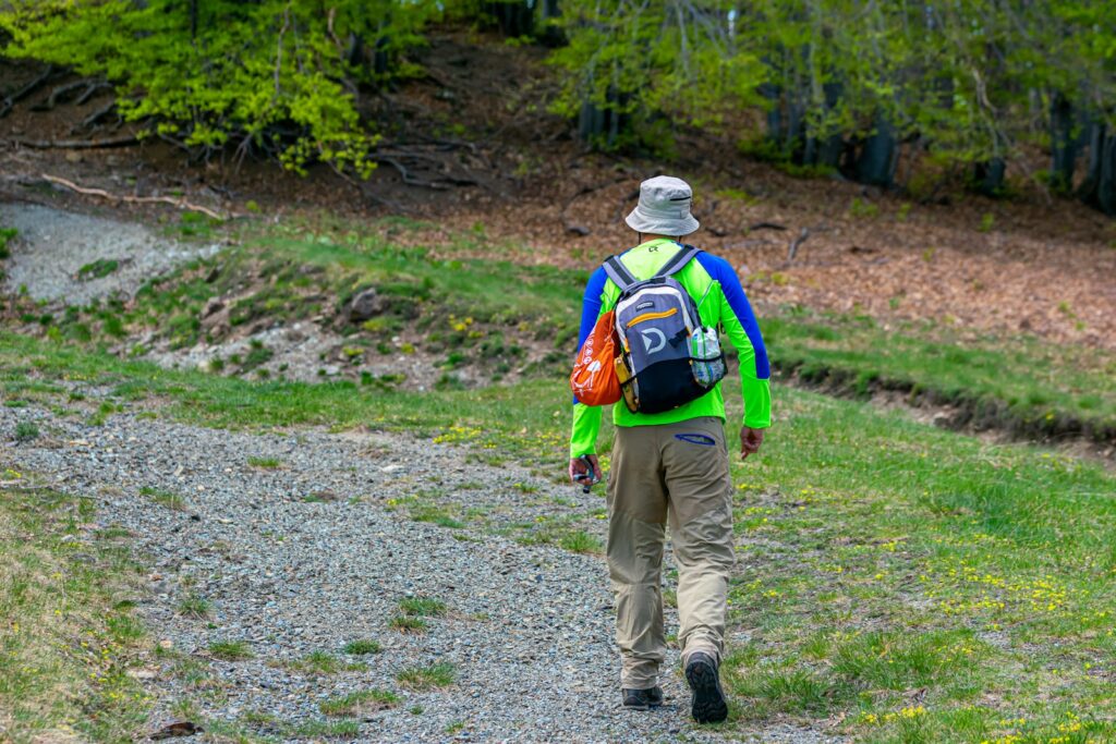 man in blue jacket and brown pants walking on dirt road during daytime