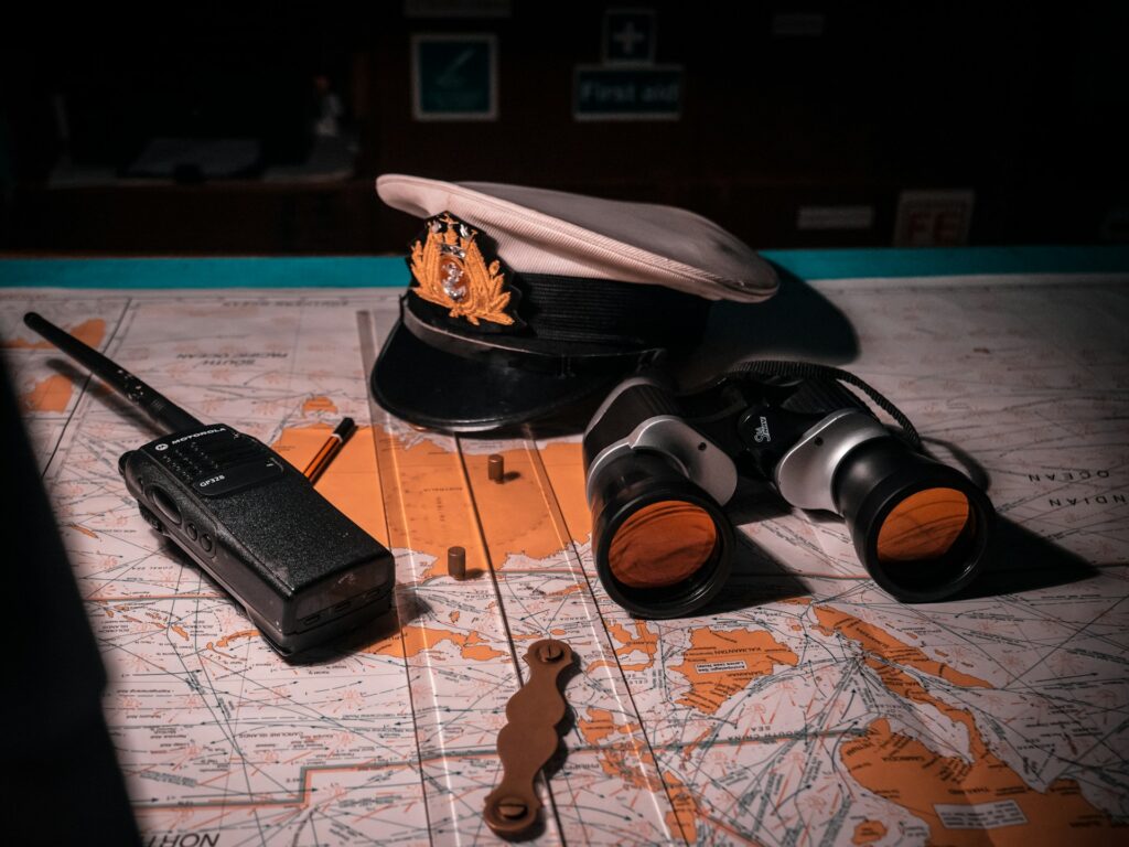 A captain's hat, binoculars, a walkie-talkie, and a map are arranged on a table, evoking a nautical exploration theme.