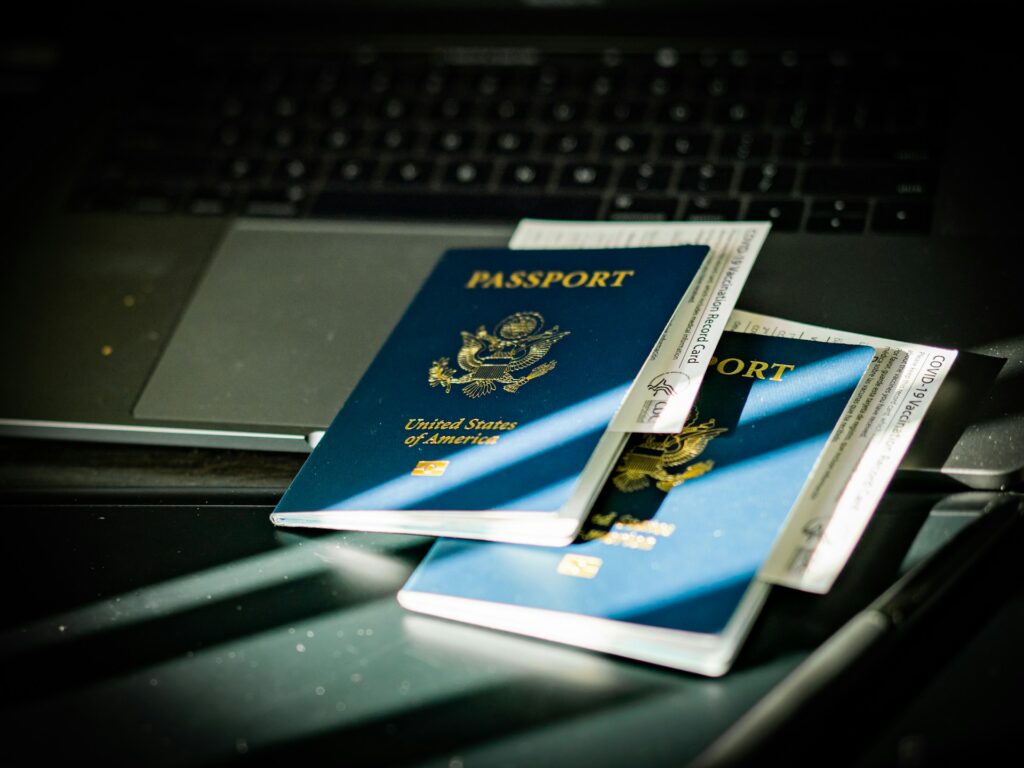Two U.S. passports and COVID-19 vaccination cards on a laptop keyboard, illuminated by soft sunlight.