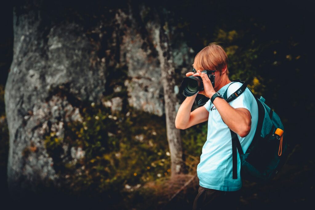 A man with a backpack is capturing a photo with a camera in an outdoor setting.