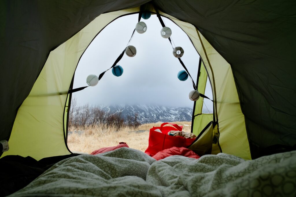 View from inside a tent showcasing cozy blankets, colorful string lights, and a scenic mountain landscape in the background.