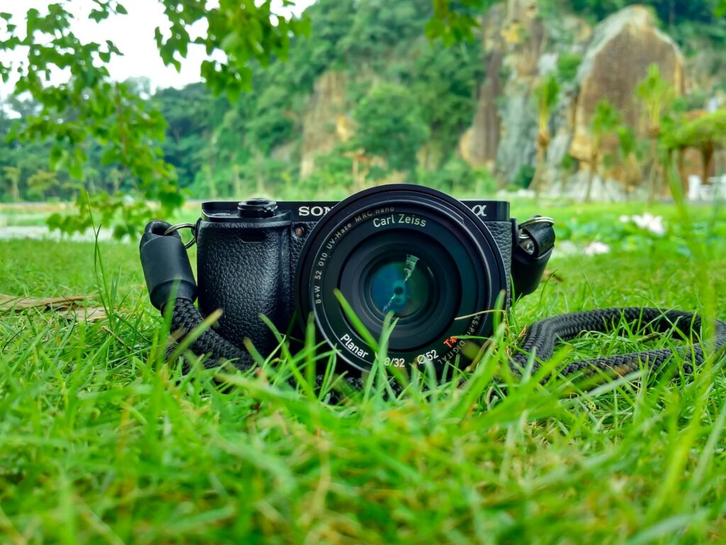 A camera rests on green grass, its strap laid beside it, capturing a moment of nature and photography.