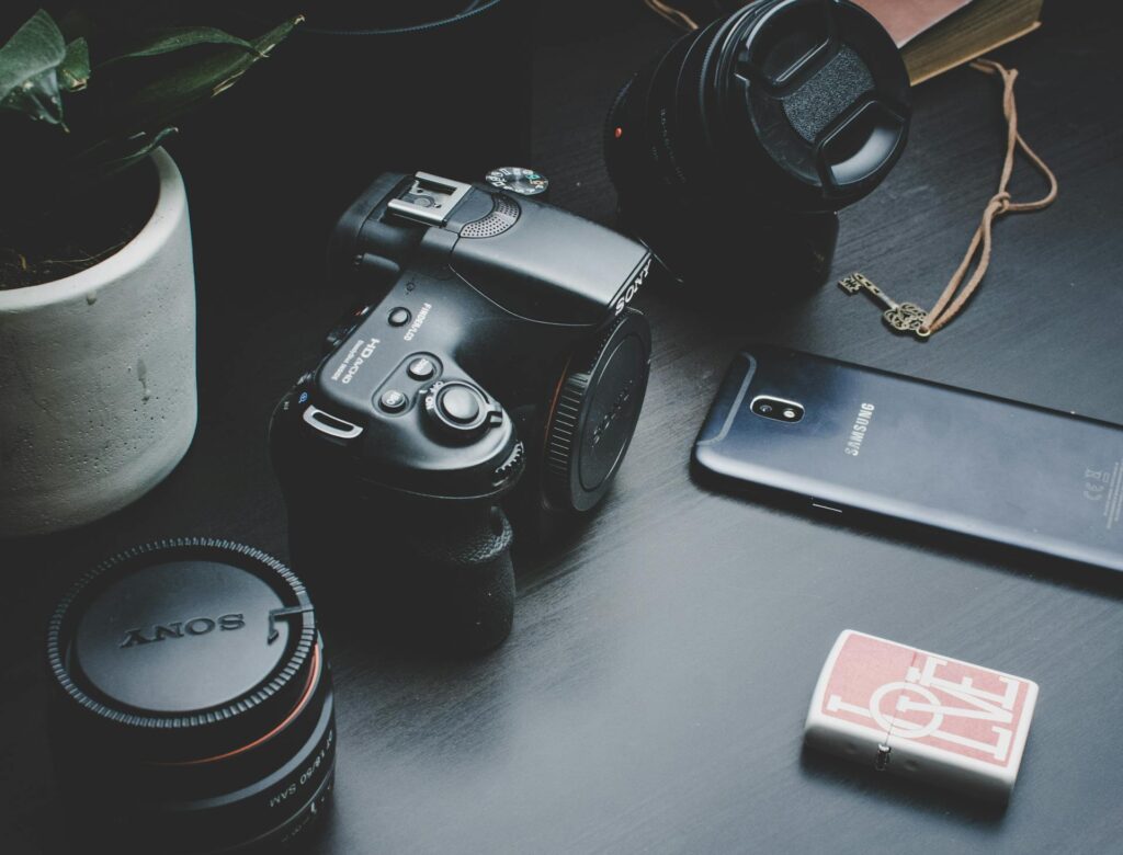 A camera, a cell phone, and a small plant are arranged on a wooden table.