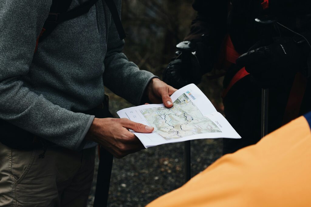 A person in a gray sweater holds a detailed hiking map, surrounded by fellow hikers preparing for an outdoor adventure.