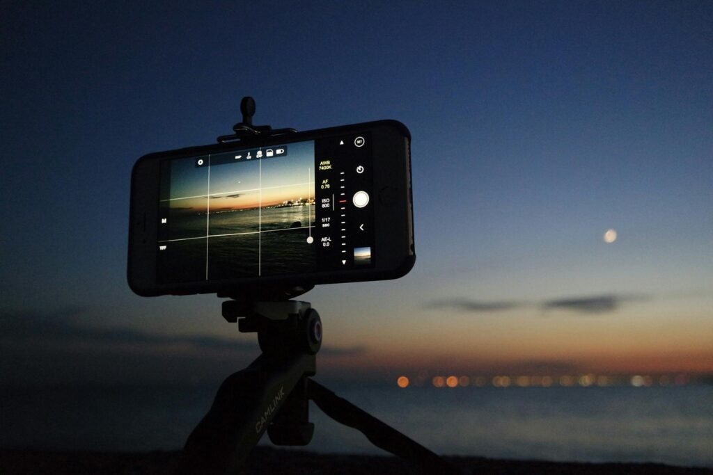 A smartphone mounted on a tripod, capturing the moon in the night sky as a backdrop.