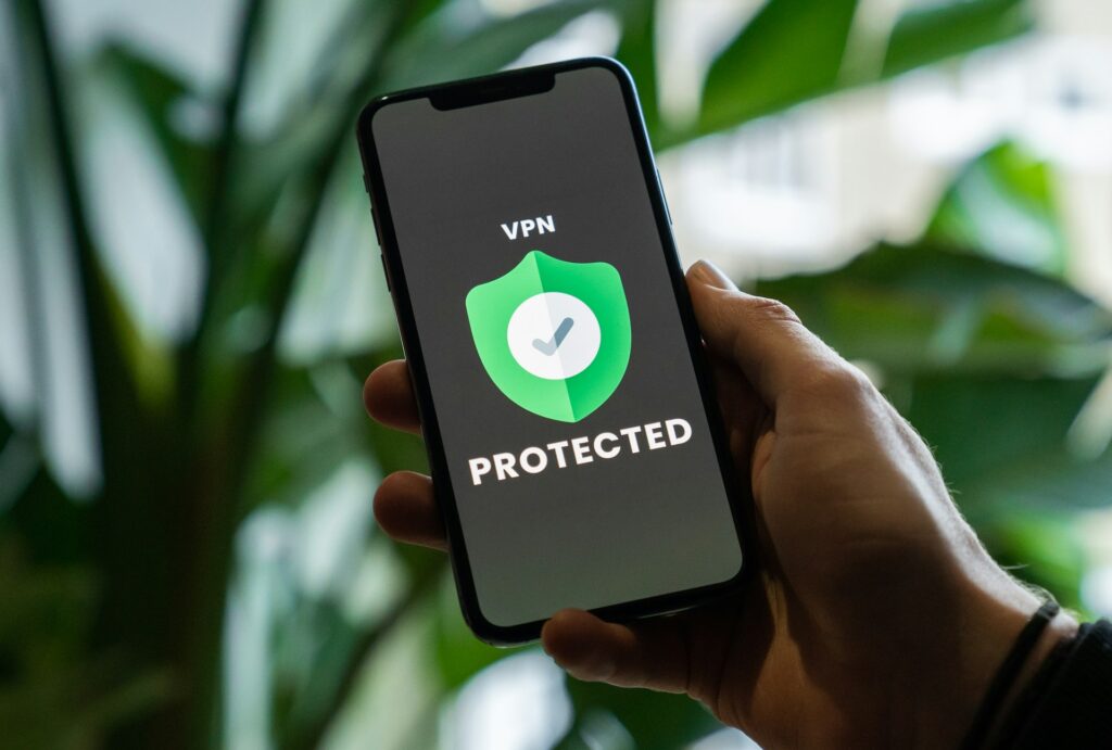 A hand holds a smartphone displaying a VPN logo with a shield and checkmark, indicating a secure and protected connection.