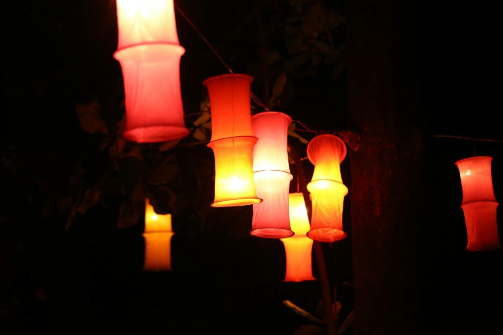 Colorful lanterns illuminating a dark night, hanging alongside each other with warm hues of red and yellow.