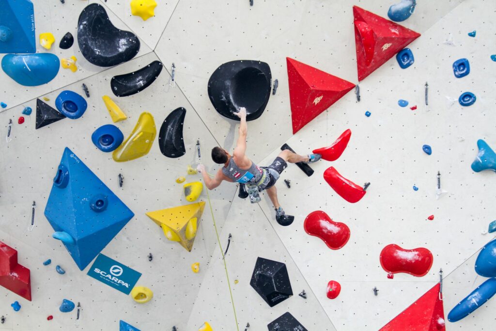 A climber ascending a colorful indoor wall with various grips, showcasing skill and determination in a bouldering competition.
