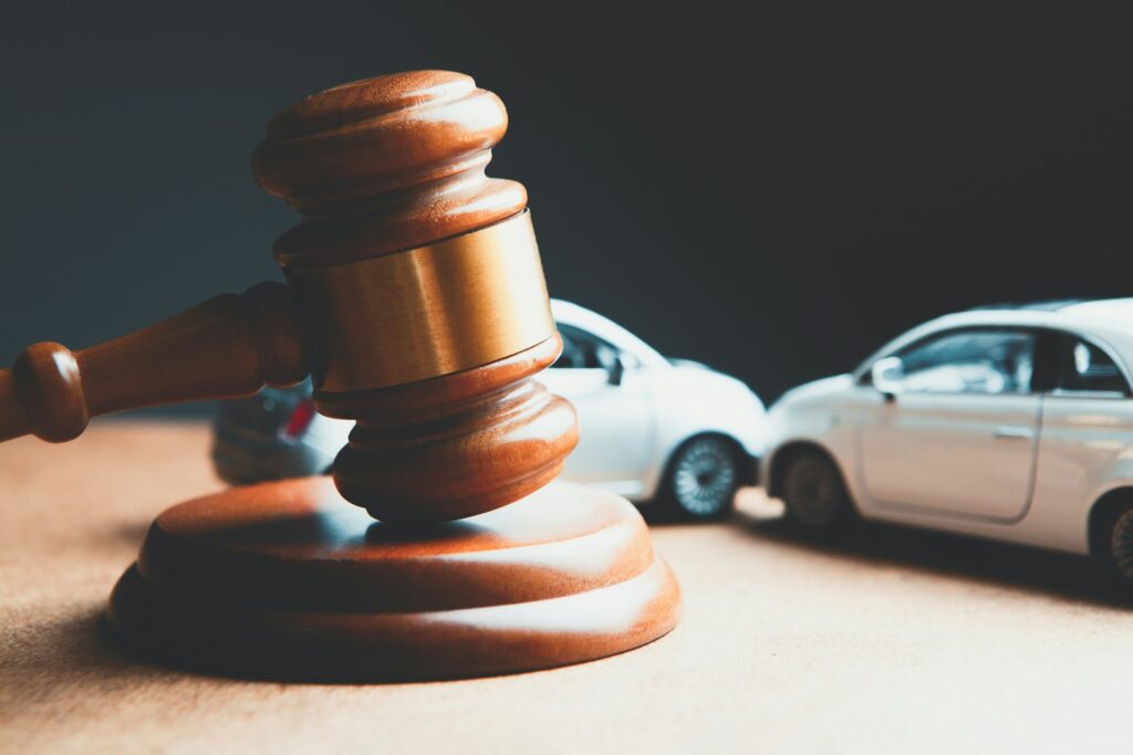 A wooden gavel positioned in front of two toy cars that appear to have collided on a neutral background, symbolizing legal matters in accidents.