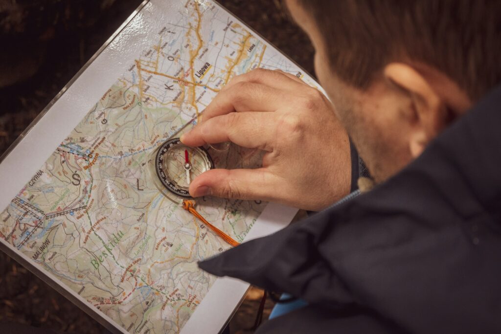 A person uses a compass on a detailed map, focusing intently on navigation in a forested area.