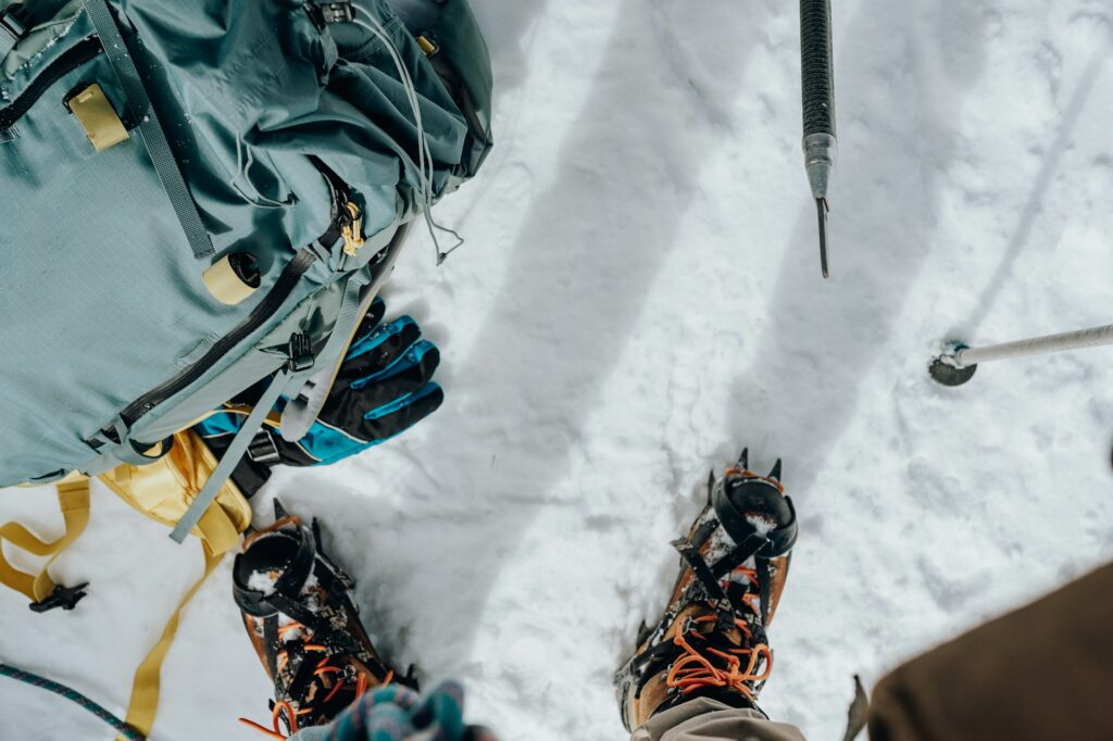 Bird's-eye view of snowy terrain, featuring climbing boots with crampons, a backpack, gloves, and climbing gear.